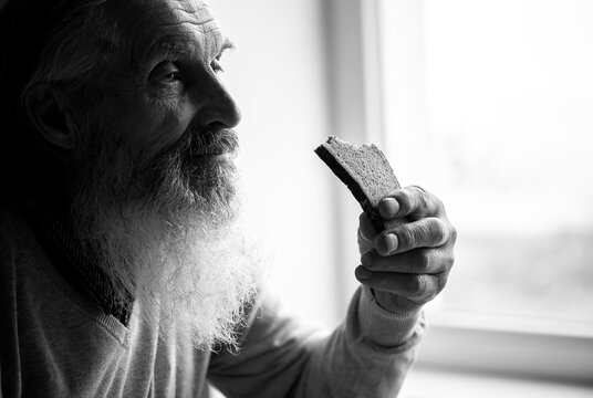 Old Sad Man With A Long Gray Beard Sitting By The Window And Eating Bread,black And White Portrait