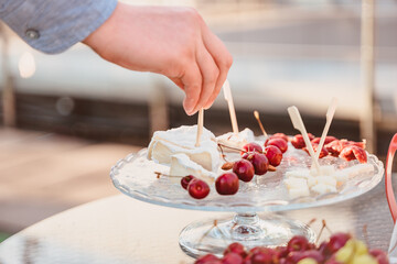 Obraz na płótnie Canvas The hand takes a canape with cheese with white mold from a glass plate with cherries