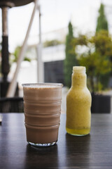 Vertical shot of delicious brown and yellow smoothies served in a cup and bottle on a sunny day