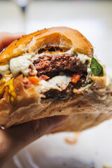 Vertical shot of a juicy burger with a bite mark in it on a blurry white background