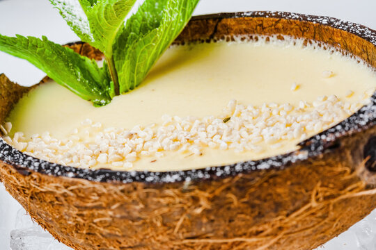 Italian dessert panna cotta with sesame seeds and mint leaves served in half coconut shell on ice cubes
