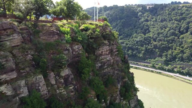 Video from a drone moving away from a cliff on the Rhine in Germany, visible road on both sides of the river.