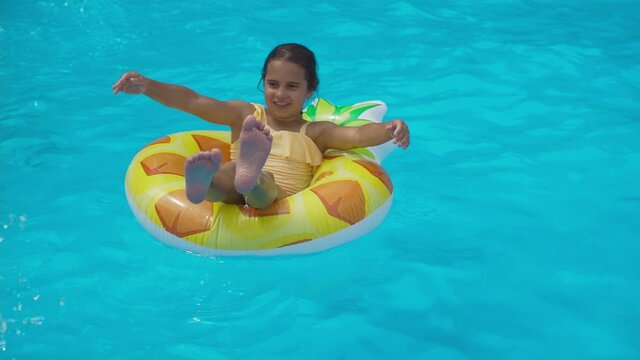 Kid dives in an inflatable pineapple ring in pool of the water park. Cheerful girl teenager plays in pool and an inflatable circle. Holidays, Vacations, Recreations, Sport, Children, Water, Hotel