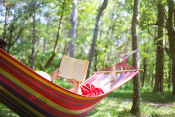 outdoor recreation. person girl or woman is lying in hammock and reading book against background of forest of trees