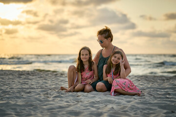 Young happy beautiful mother and her daughters on the beach at sunset. 