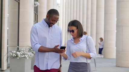 African business couple walking outdoors and using smartphone