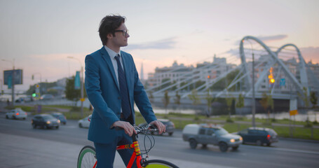 Portrait of young businessman in smart casual clothes standing near bike on city street