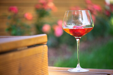 A glass of chilled cold white wine with strawberries on an outdoor wooden terrace
