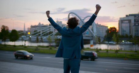 Fototapeta na wymiar Rear view of businessman raising arms up to sky in city celebrate success.