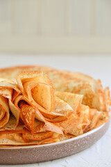 Traditional Russian Crepes Blini stacked in a white plate on light background. Maslenitsa...