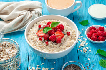 Oatmeal porridge with fresh berries and chia seeds on a blue background. Side view, close-up.