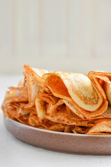 Traditional Russian Crepes Blini stacked in a white plate on light background. Maslenitsa...