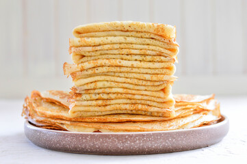 Traditional Russian Crepes Blini stacked in a white plate on light background. Maslenitsa traditional Russian festival meal. Russian food, russian kitchen