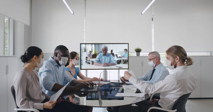 Smart business team in face mask have online video call on monitor in office