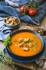 Tomato cream soup with pine seeds and croutons on a wooden table, vertical