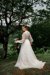 Fototapeta premium A bride in a white dress stands at the trees in the mountains
