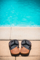 Close-up of a pair of flip-flops or thongs in front of a swimming pool. Summer and holidays concept with copy space.