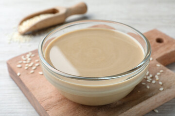 Tasty sesame paste in glass bowl on wooden board, closeup