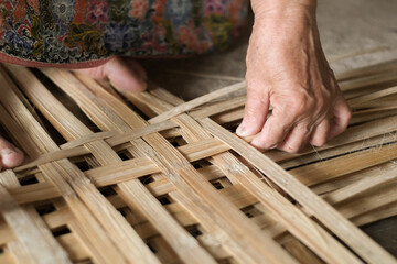 Hand elderly woman are weave bamboo strips of bottom of basket bamboo close-up.