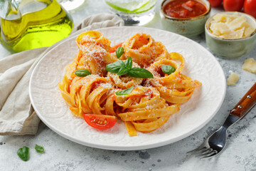 Tasty appetizing classic italian tagliatelle pasta with tomato sauce, cheese parmesan and basil on plate on light table. View from above, horizontal