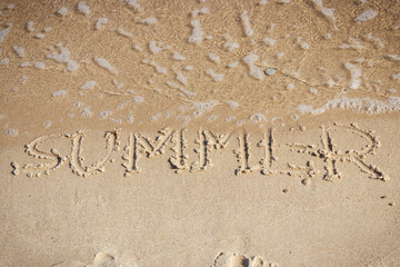 Inscription summer and incoming sea wave on sand at beach. Travel and vacation time