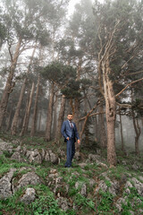 attractive man with beard in business suit stands in the mountain forest