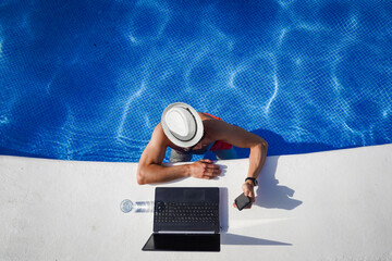 bird view of remote online working digital nomad man on workation with hat &  laptop at a white...