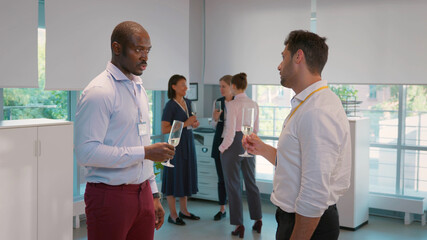 Fototapeta premium Side view of cheerful multicultural businessmen holding champagne glasses and talking in office