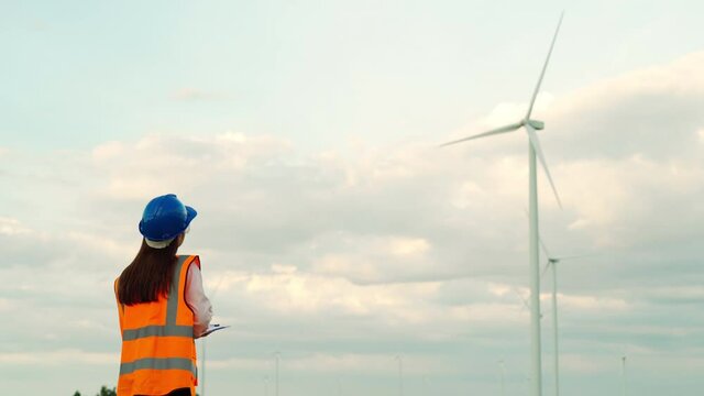 female engineer working and writing on clipboard against wind turbine farm