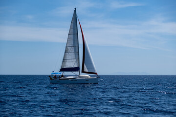 Sailing boat with open white sails, blue sky and rippled sea background