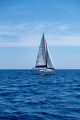 Naklejka premium Sailing boat with open white sails, blue sky and rippled sea background