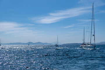 Sailing boats with open white sails, blue sky and rippled sea background