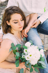 beautiful pensive bride sits next to the groom holding a white bouquet of flowers.