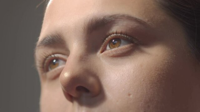 No make up caucasian girl looking aside and blinking. Close up brown eyes. Studio still shot with dramatic light close-up low angle portrait high quality video.