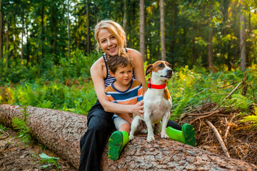 Beautiful blond hair mothe sits on log with son and a dog in the forest