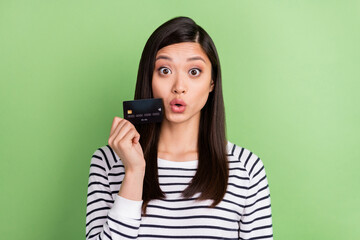 Fototapeta premium Portrait of attractive amazed funky girl holding in hands bank card staring pout lips news isolated over green color background