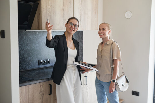 Waist Up Portrait Of Female Real Estate Agent Giving Apartment Tour To Young Woman Buying New House