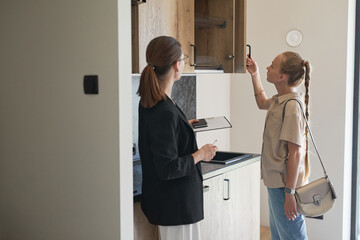 Waist up portrait of female real estate agent giving apartment tour to young woman buying new house