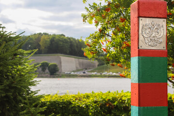 Red-green striped border post with a coat of arms of Russia. Double-headed eagle. Narva River. Border control