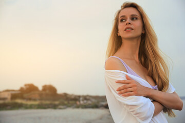 Fototapeta na wymiar Beautiful young woman on beach in evening, space for text