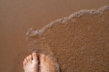 Women standing on the clean sandy beach with wave motion coming to their feet. Top view of woman...