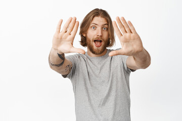 Excited blond guy look through hand frames and smiling amused, shooting, creating picture, imaging something, being inspired, standing over white background