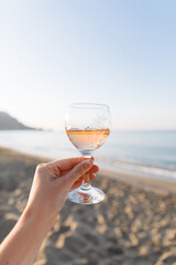 Summer picnic on the beach at sunset. Young woman with glass of rose wine. Weekend picnic. Close up.