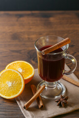 Mulled wine in glass cups with cinnamon and oranges on a wooden table.