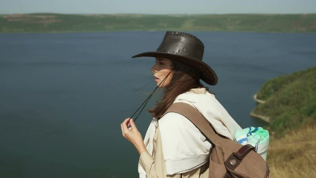 Attractive woman with long dark hair with backpack enjoying amazing view of Bakota bay. Happy tourist in cowboy hat spending weekends at national park.