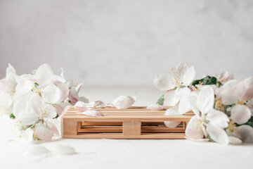 Fototapeta na wymiar Wooden podium in form of pallet on light plaster surface with apple flowers. Pedestal or stage. Mockup for cosmetic