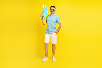 Full size photo of funny brunet man with gun wear t-shirt shorts isolated on yellow color background