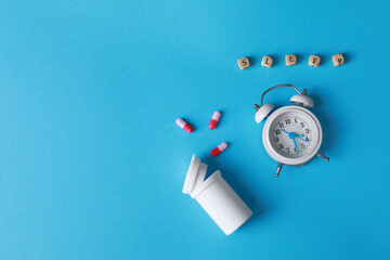 Alarm clock, pills near word Sleep made of cubes on light blue background, flat lay. Insomnia treatment