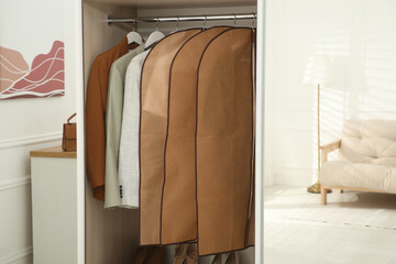Garment bags with clothes on rack in wardrobe indoors