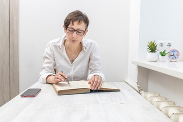 Middle-aged woman with short-haired brunette in glasses reads the book, sitting at the table